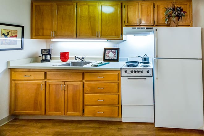 A cozy kitchen with wooden cabinets, a stove, refrigerator, and countertop space.