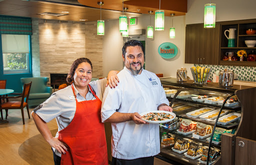 Two chefs proudly present a dish in a vibrant restaurant setting.