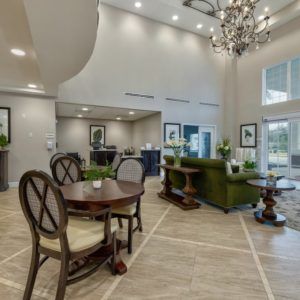 A spacious and elegantly furnished living area with a high ceiling, featuring a chandelier, dining table, and comfortable seating.