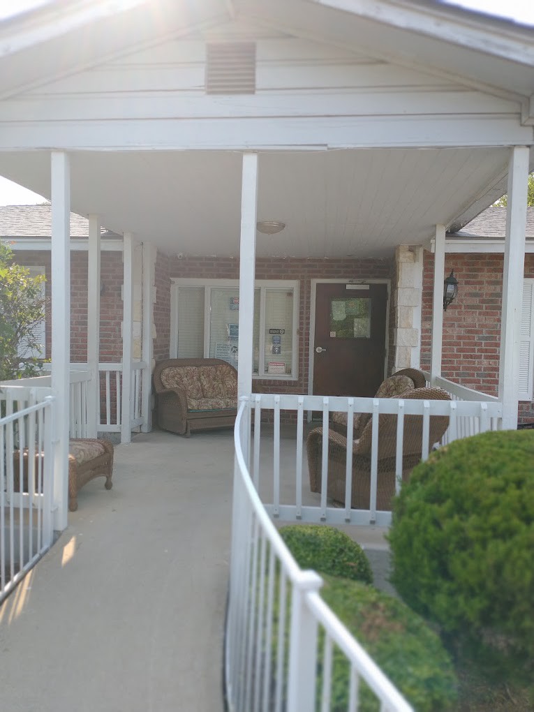 A covered porch with a ramp, featuring outdoor seating and a brick wall.