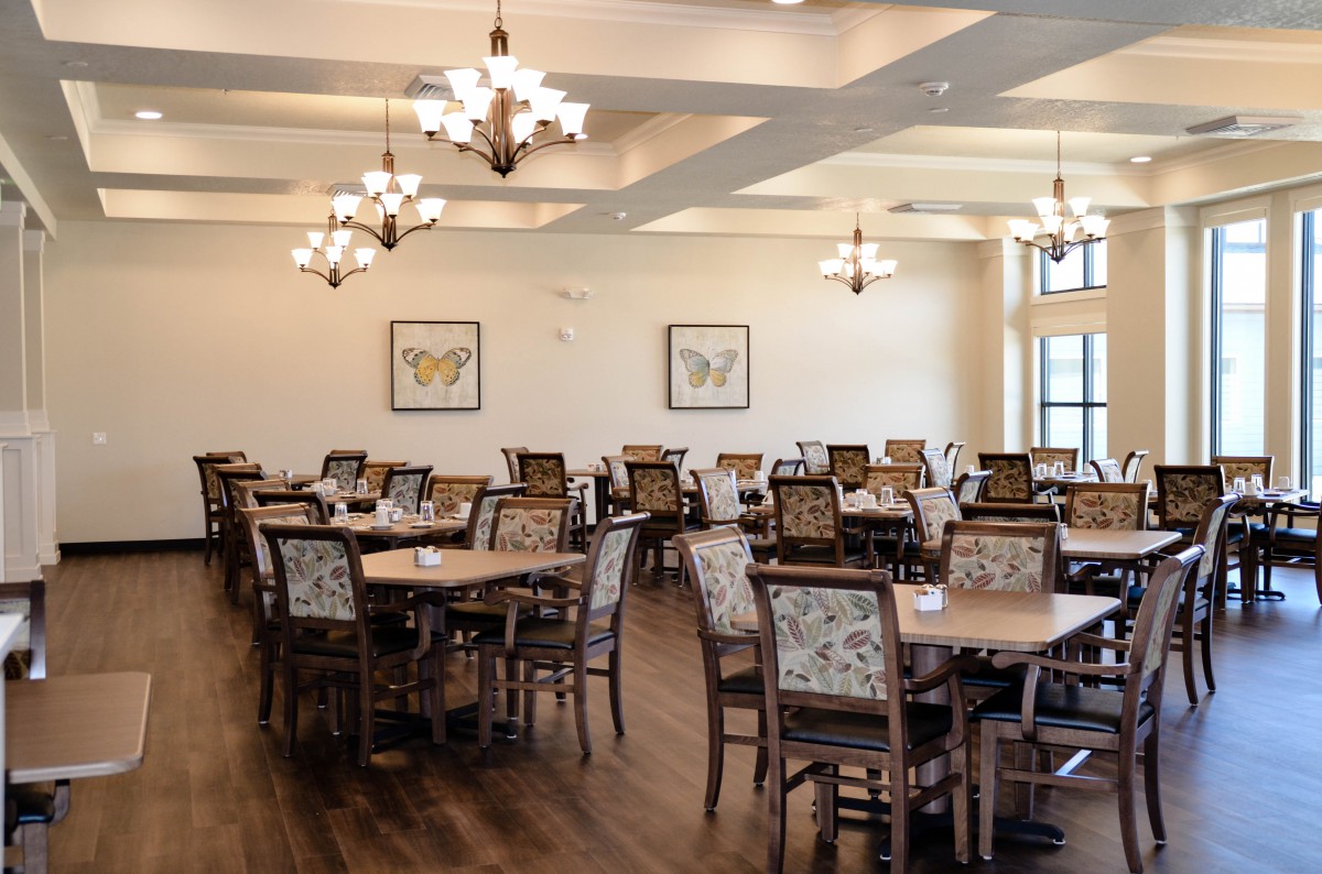 A well-lit dining area with several tables and chairs arranged neatly, featuring elegant chandeliers and wood flooring.
