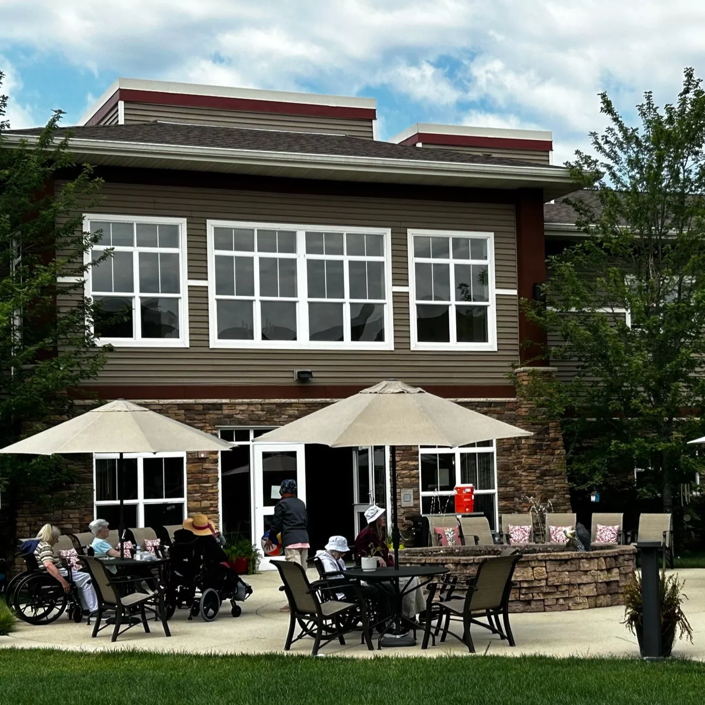 A group of people sitting under umbrellas on a patio in front of a two-story building.