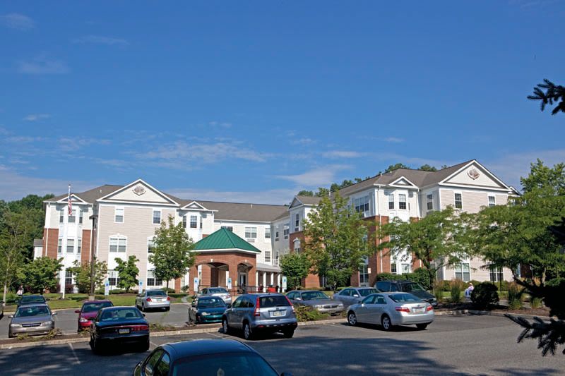 A residential apartment complex with a parking lot filled with cars on a sunny day.