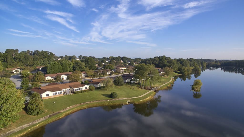 An aerial view of a serene lakeside community with houses, lush greenery, and clear skies.