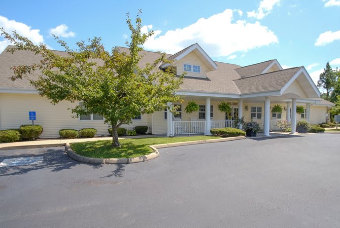 A sunny view of a house with a tree in the front yard and a spacious parking lot.