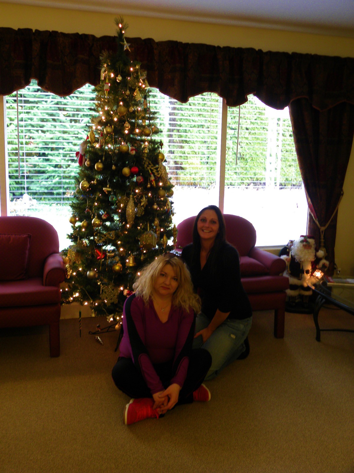 Two people sitting by a decorated Christmas tree in a cozy living room.