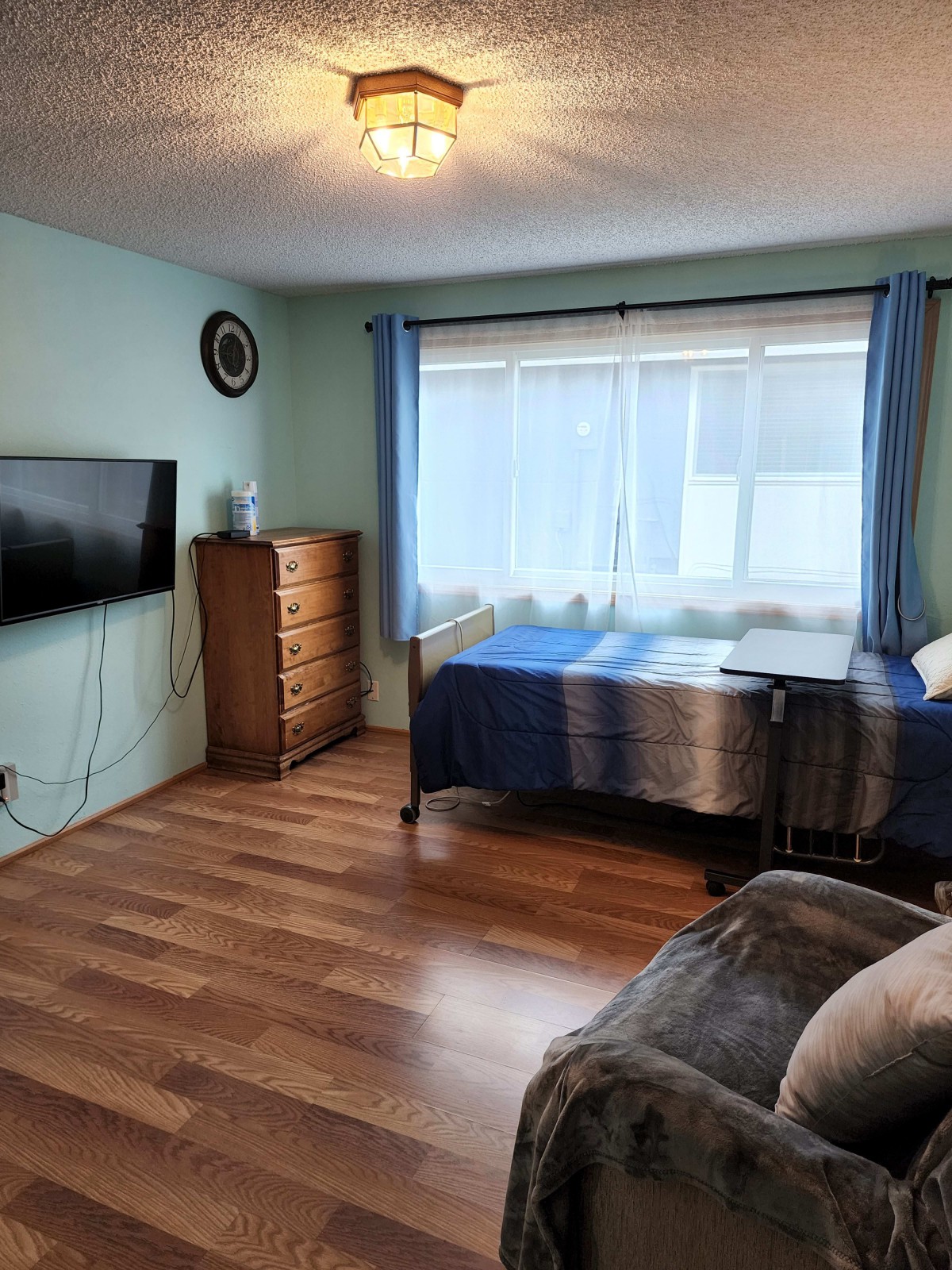 A cozy bedroom with a bed, dresser, and wall-mounted TV.