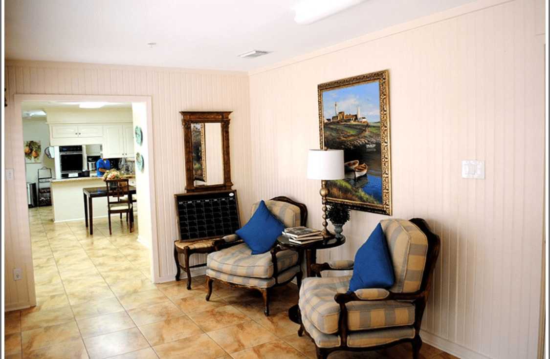 A cozy living room corner with two upholstered chairs, a side table with a lamp, and artwork on the wall.