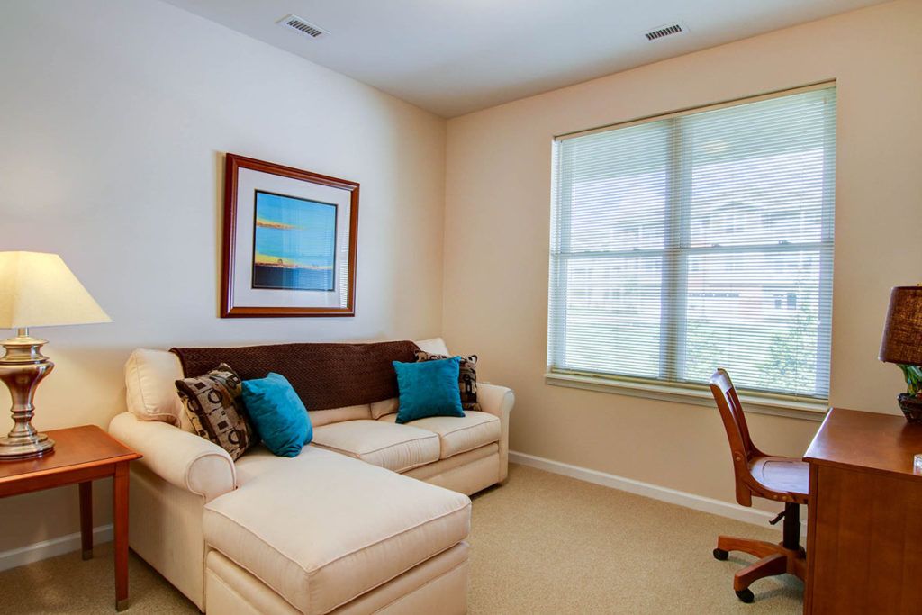 A cozy living space with a white couch, colorful pillows, artwork on the wall, and a window letting in natural light.