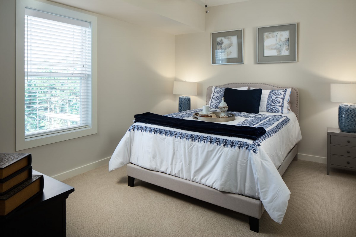 A cozy bedroom with a neatly made bed, decorative pillows, and a lamp by the window.