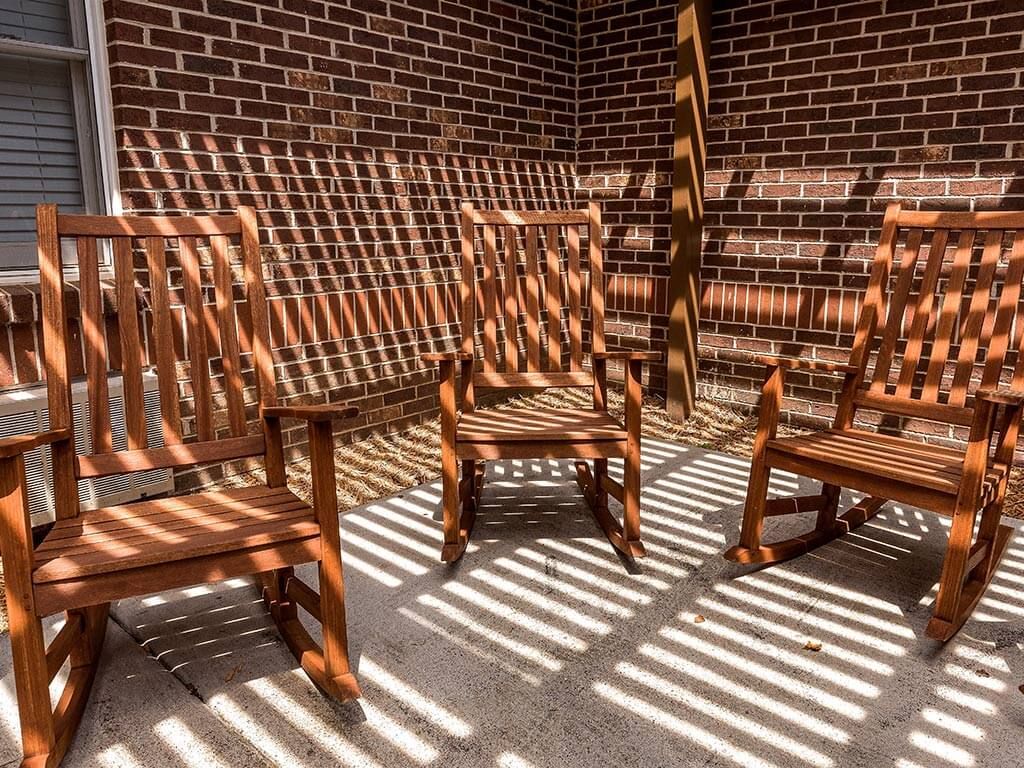 Wooden chairs casting intricate shadows under the sun against a brick wall.