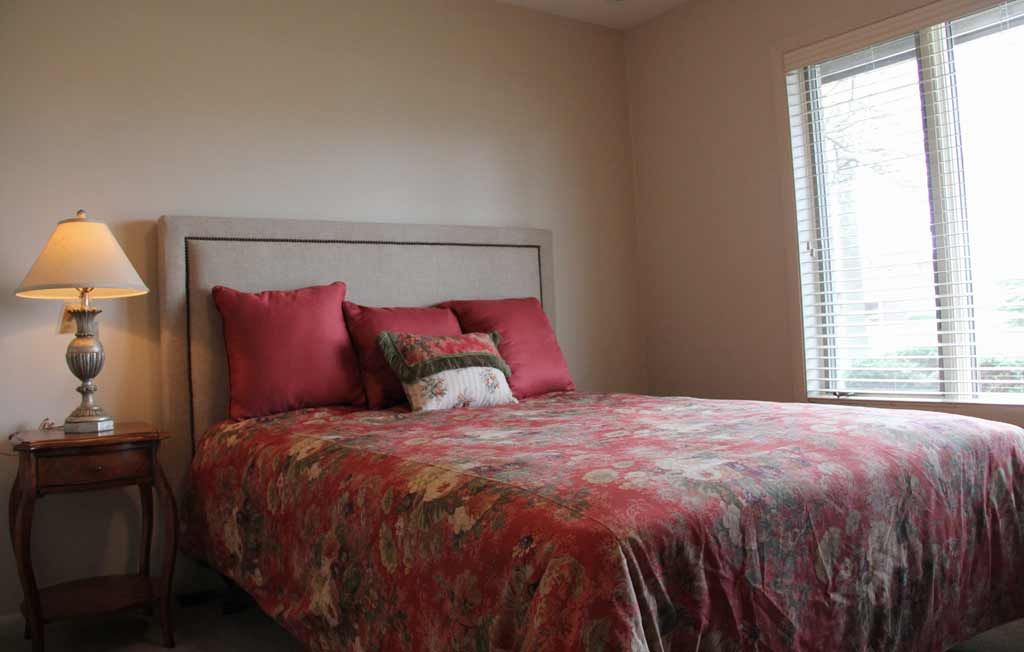 A cozy bedroom featuring a bed with a colorful comforter and pillows, beside a window.