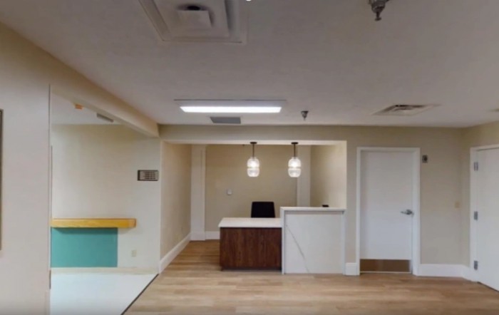 A modern office reception area featuring a central desk with pendant lighting and wooden flooring.