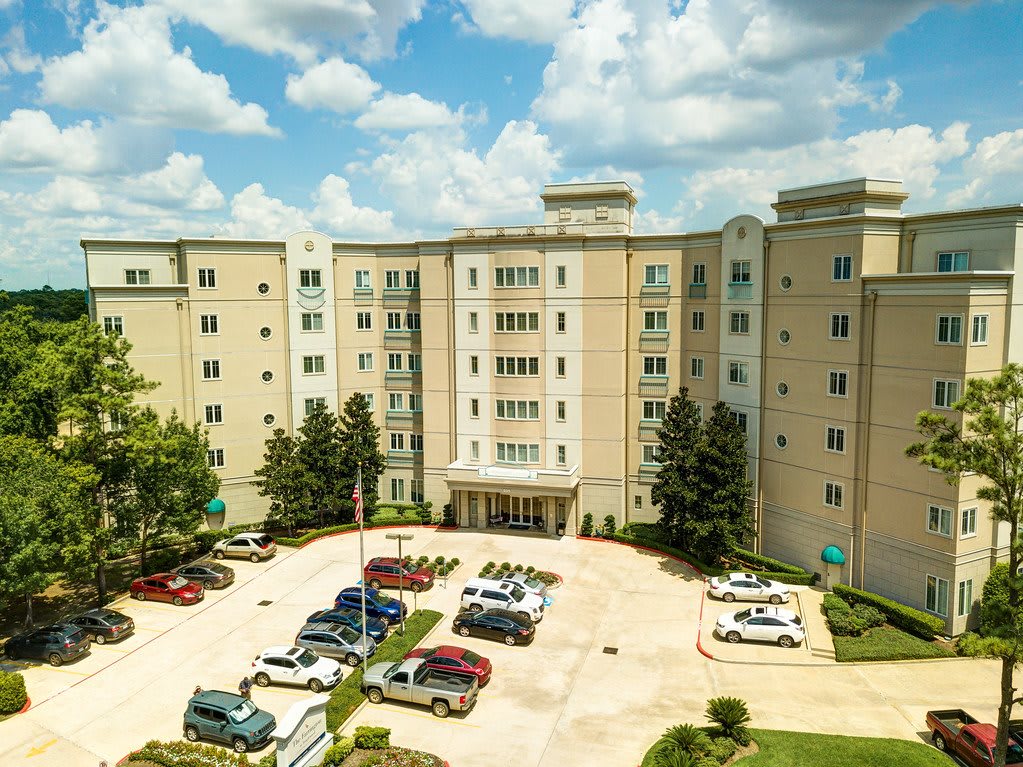 A multi-story residential building with a parking lot and trees under a cloudy sky.