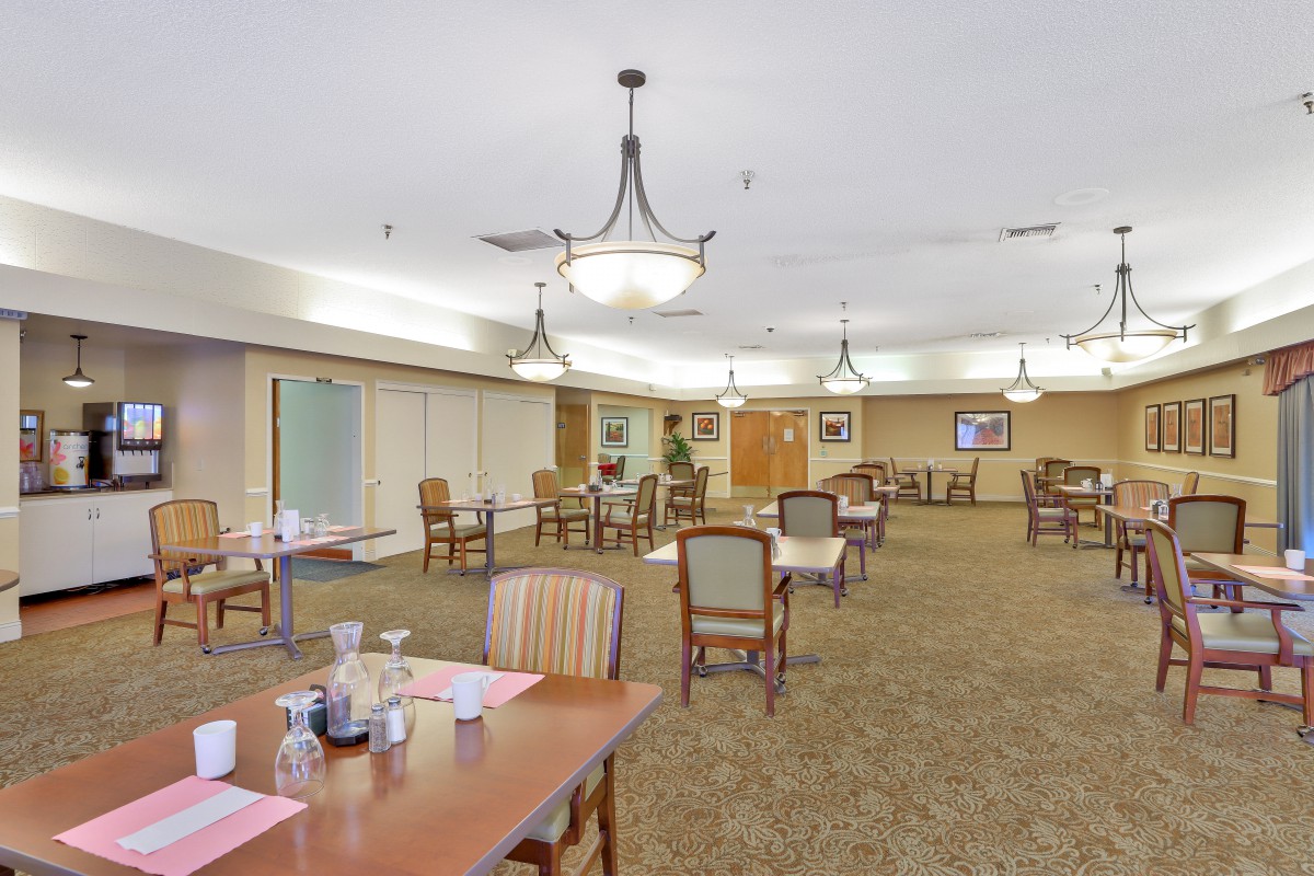 A spacious dining room with neatly arranged tables and chairs, featuring elegant chandeliers hanging from the ceiling.