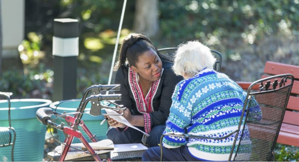 A caregiver speaking with an elderly person outdoors.