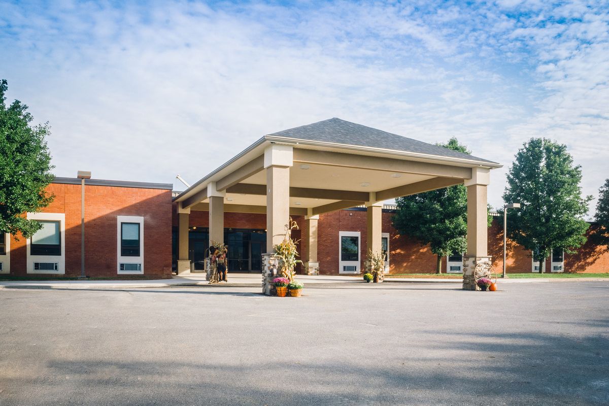 A brick building with a large entrance canopy and decorated with plants.