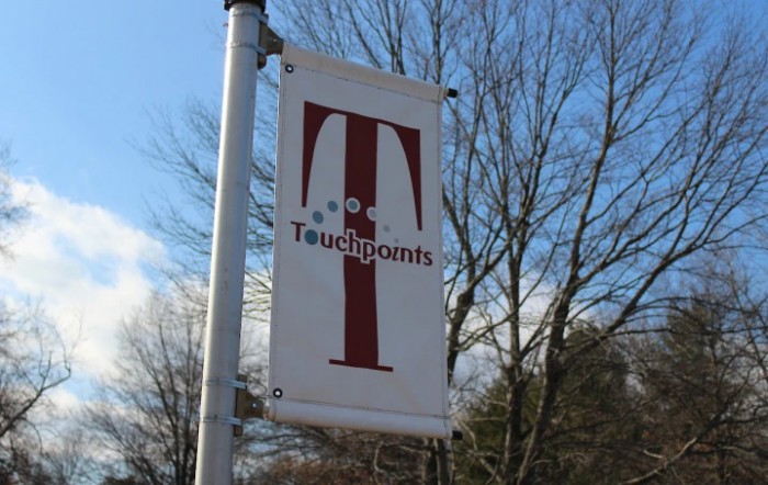 A vertical sign with a logo and text reading 'Touchpoints' against a backdrop of trees and sky.