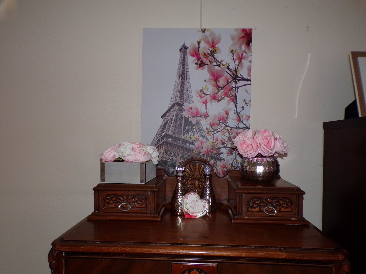 A beautifully decorated wooden dresser with floral arrangements and a painting of the Eiffel Tower.