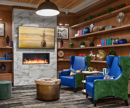 A modern and cozy living room with vibrant blue armchairs, a fireplace, and bookshelves.