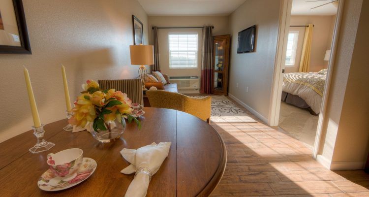 A cozy living room with a round table, lamp, and sofa under natural light from a window.