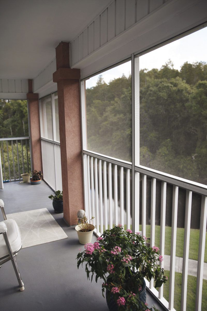 A cozy balcony with potted plants and seating, overlooking a lush green landscape.