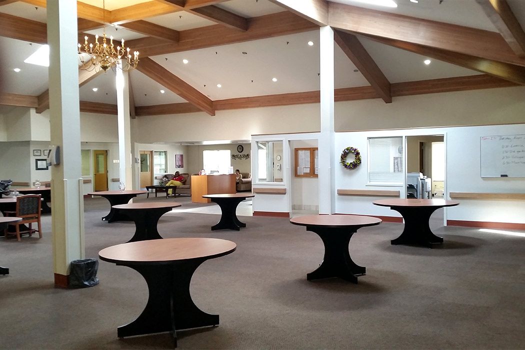 Spacious banquet hall with round tables, a chandelier, and exposed ceiling beams.