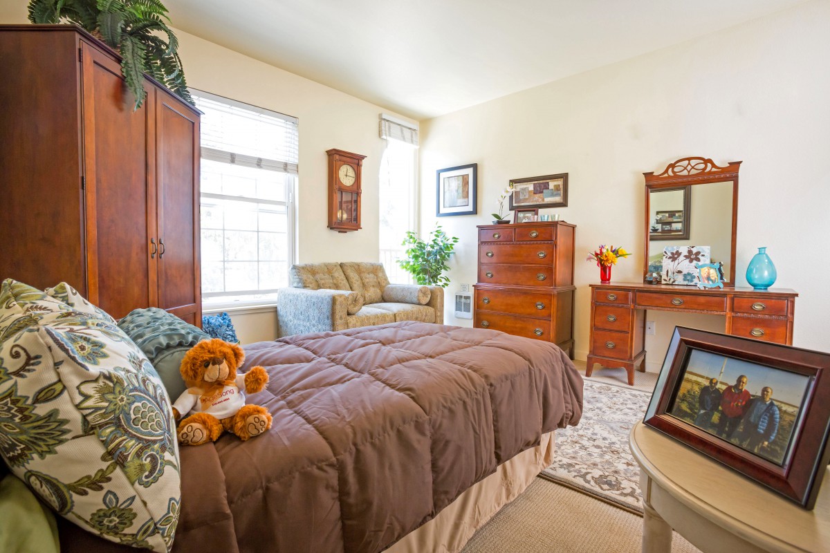 A cozy bedroom with warm tones, featuring a bed, dresser, and comfortable chair.