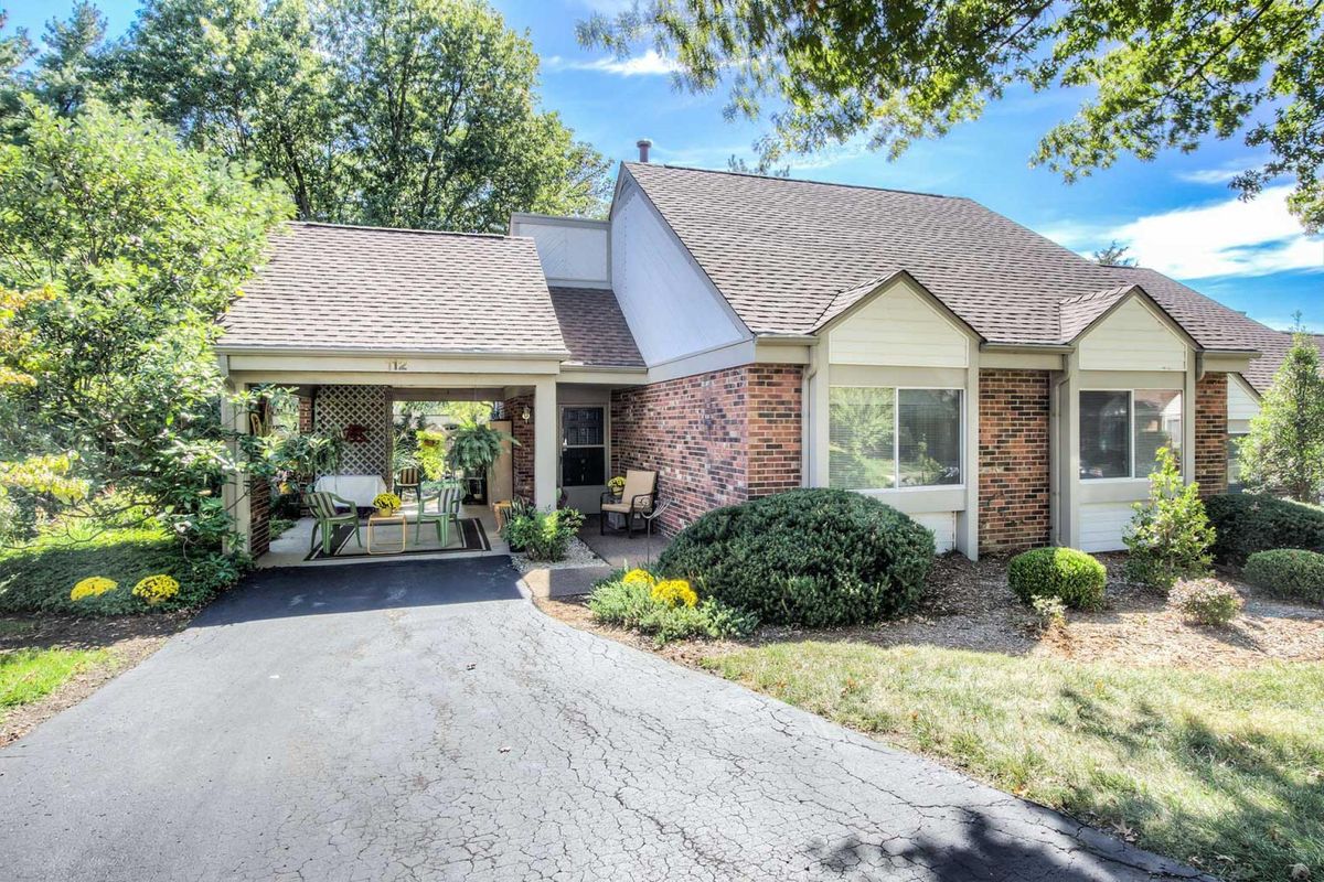 A suburban house with a brick exterior and a well-maintained driveway surrounded by trees and landscaping.