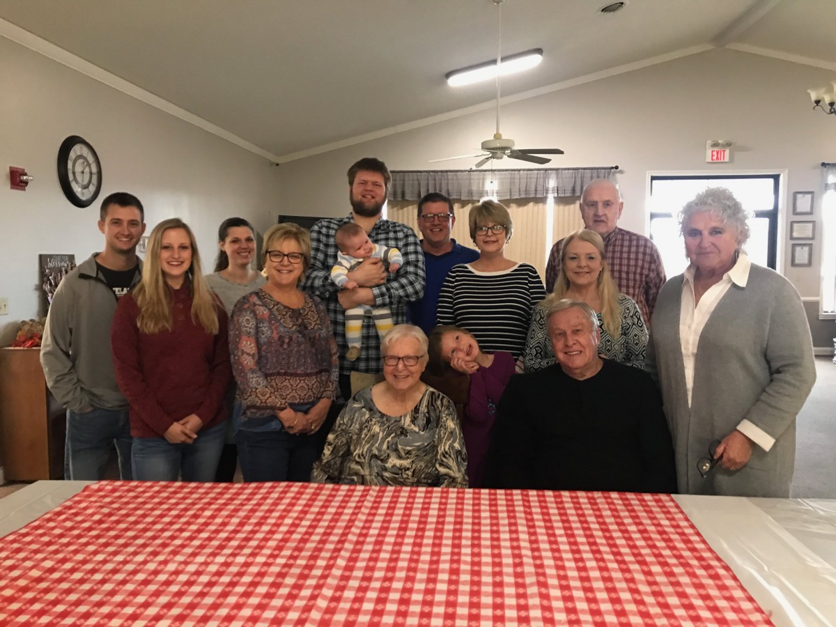 A family gathering with multiple generations posing for a group photo indoors.