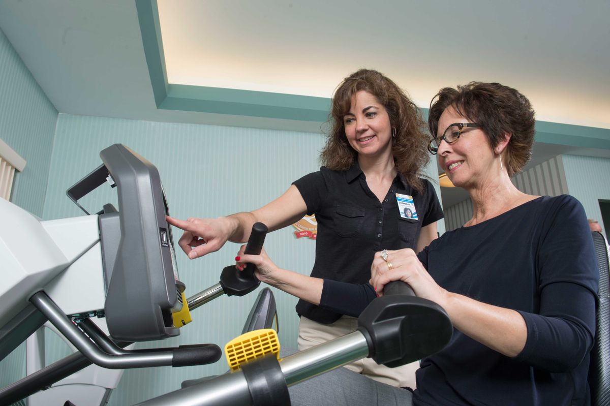 A trainer assists a woman during her workout on a treadmill.