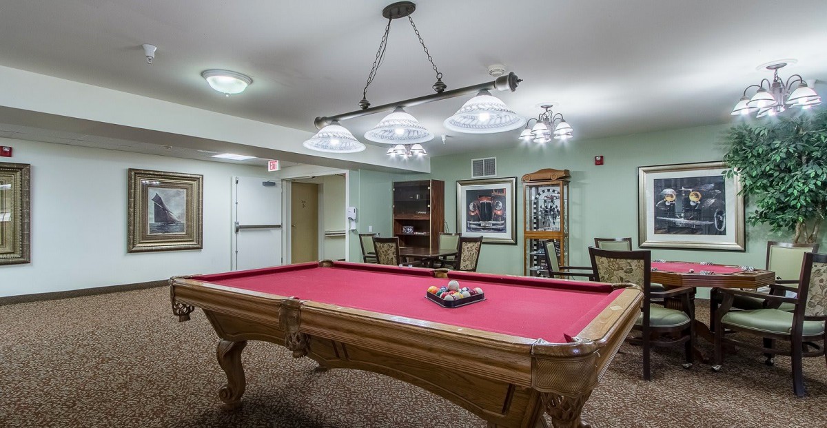 A cozy game room featuring a red-felt pool table under elegant lighting.