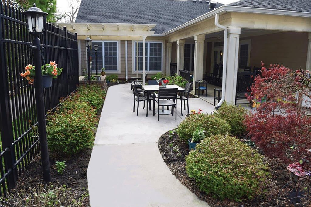 A serene patio setup with a pathway leading to outdoor furniture surrounded by lush landscaping.