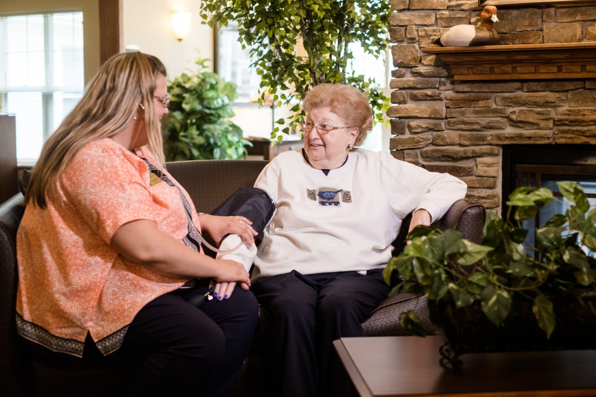 A nurse assists an elderly woman in a cozy indoor setting.