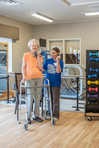 An elderly woman receiving support during a rehabilitation exercise session.