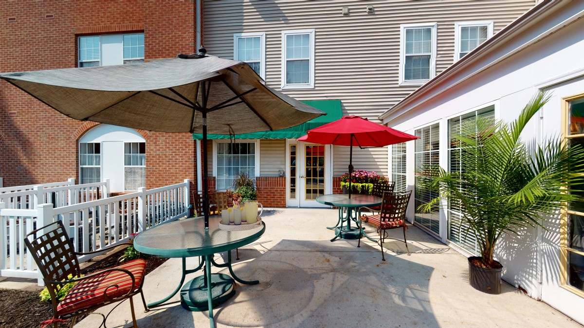A cozy patio area with tables and chairs under colorful umbrellas, set against the backdrop of a building exterior.