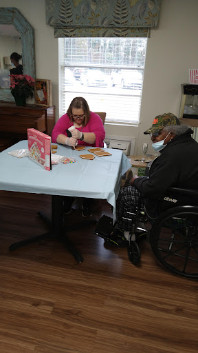 A caregiver engages in a craft activity with an elderly individual in a wheelchair, fostering connection and creativity.