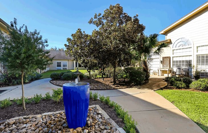 A beautifully landscaped garden with a striking blue fountain and winding pathways under a clear, sunny sky.