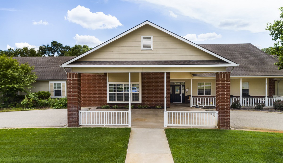 A charming single-story house with a brick exterior and a welcoming front porch surrounded by a well-kept lawn.