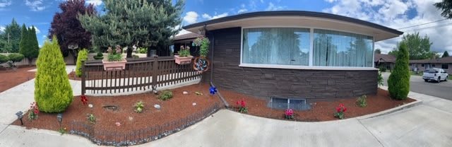 A house with a small garden featuring hanging plants and a flower pot, adjacent to a driveway.