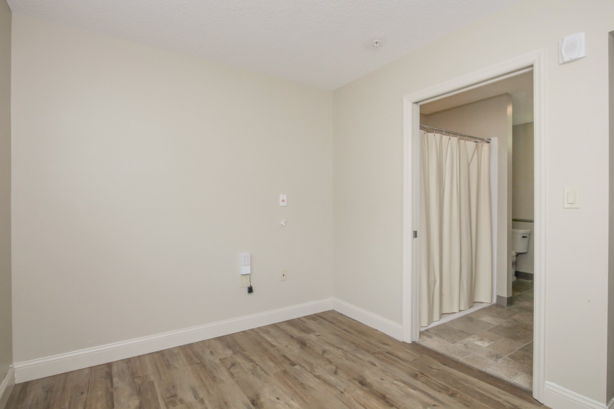 An empty room with hardwood floors and beige walls, featuring a doorway with curtains.