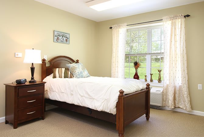 A cozy bedroom with a neatly made bed, wooden furniture, and natural light streaming through the window.