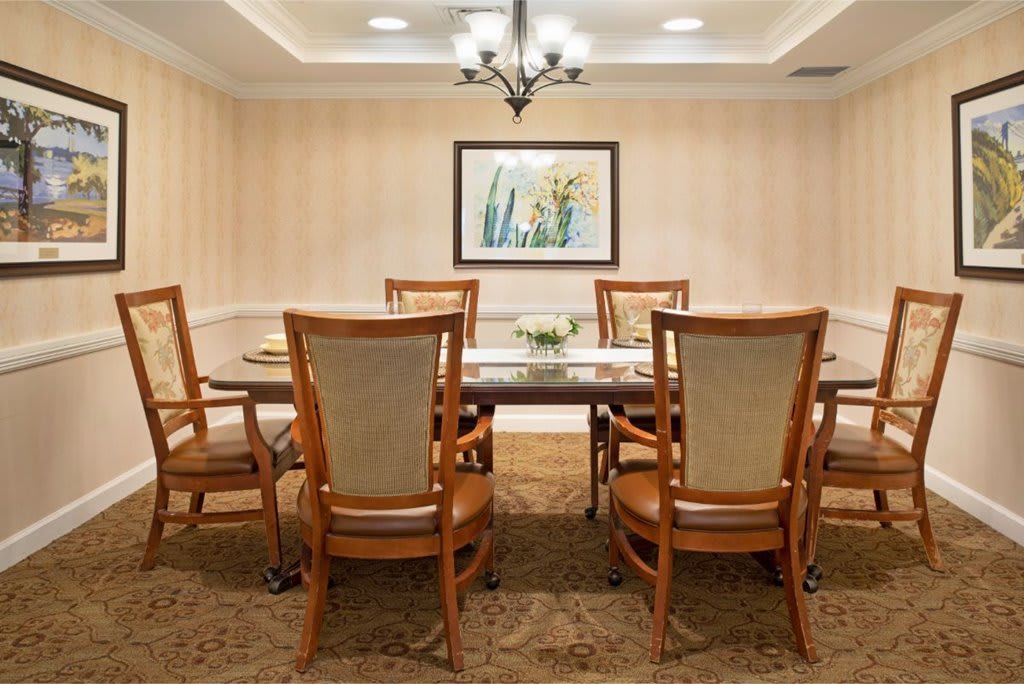 A well-decorated dining room with a large table, six chairs, and a chandelier overhead.