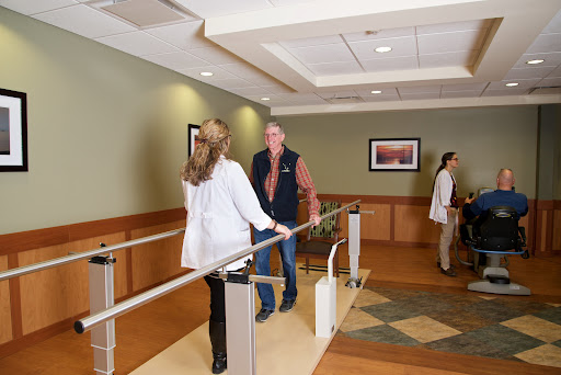 A physical therapy session in a healthcare facility, with a patient practicing walking with the assistance of medical staff.