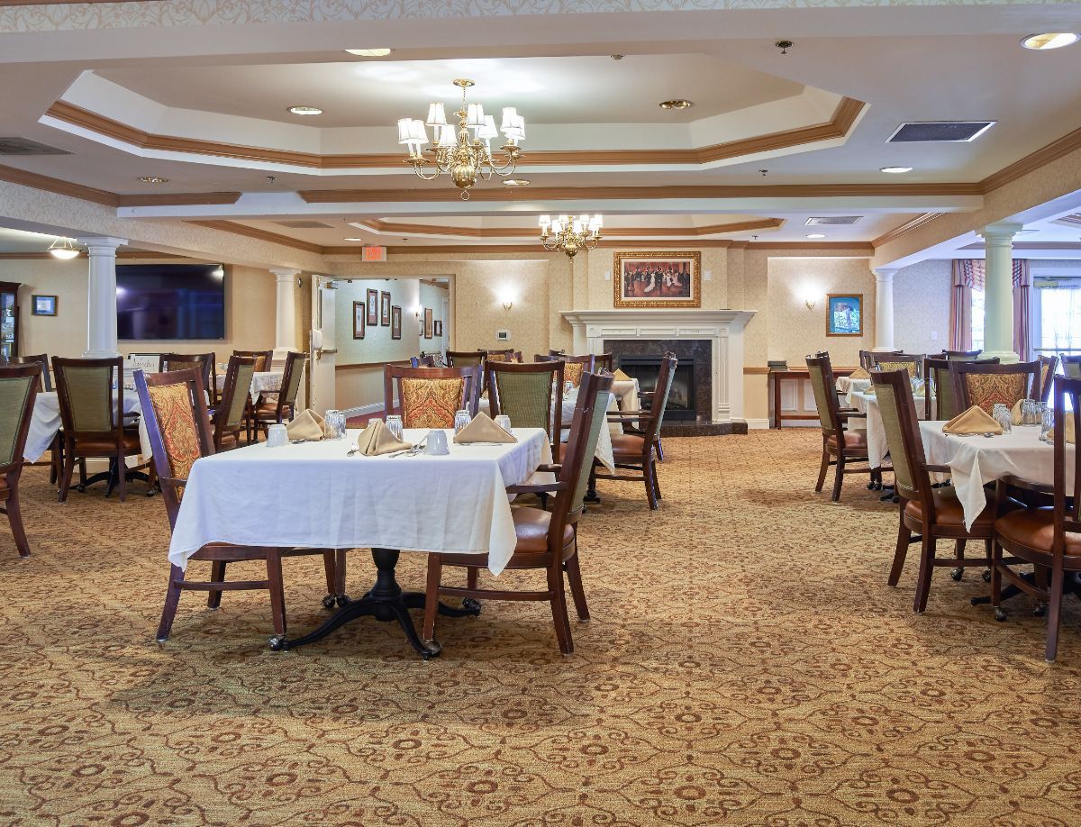 An elegantly arranged dining area with tables and chairs, adorned with chandeliers and a carpeted floor.