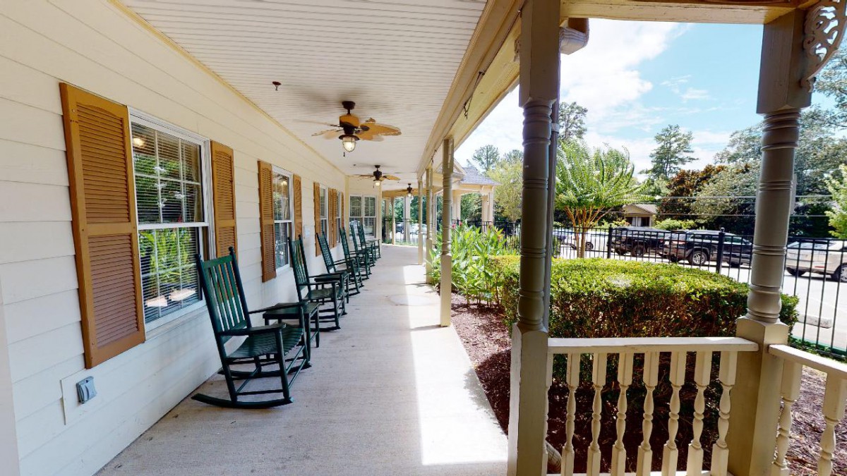 A long porch with a row of rocking chairs and ceiling fans, overlooking a garden.