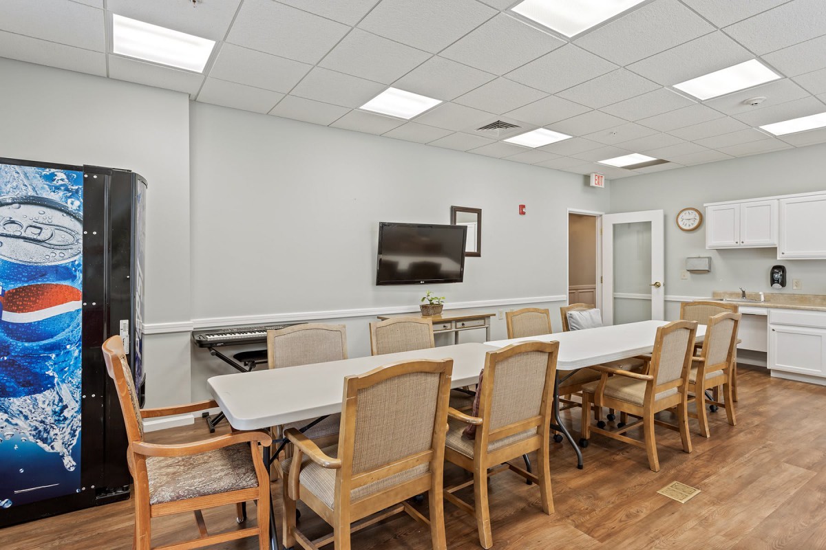 A modern conference room with a long table, office chairs, and a wall-mounted television.