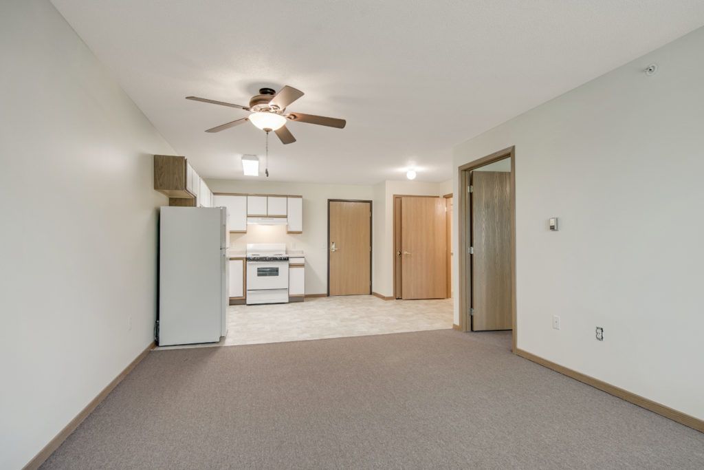 An empty apartment interior featuring a kitchen and living area with a ceiling fan.