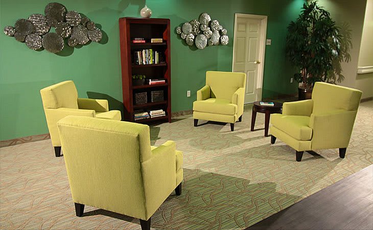 A cozy living room featuring lime green armchairs, a bookshelf, and decorative wall art.