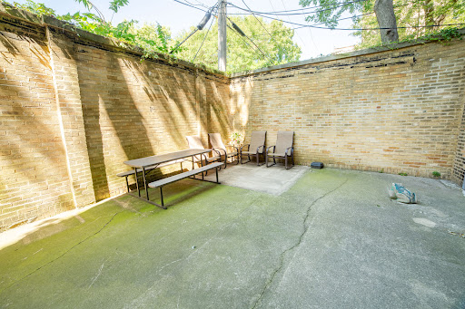A secluded outdoor seating area with benches and chairs, surrounded by walls and dappled sunlight.